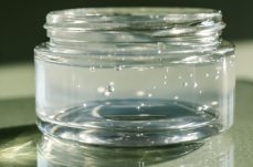 Transparent cosmetic gel in a jar on a green background in a beam of light.